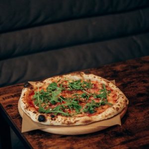A freshly baked wood-fired pizza topped with arugula served on a rustic wooden table.