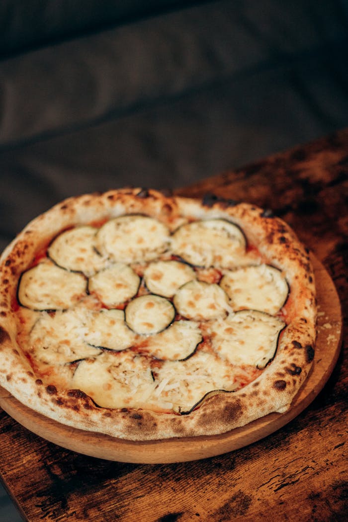 Mouth-watering wood-fired pizza topped with zucchini and melted cheese on a rustic wooden table.