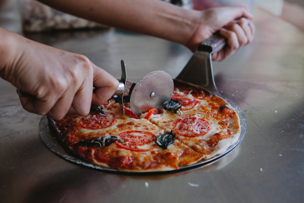 A person slicing a delicious, freshly baked pizza with a pizza cutter, showcasing vibrant toppings.